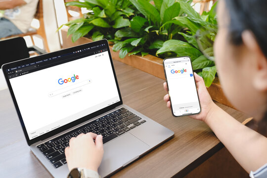 Bangkok, Thailand. November 18, 2024; Person accessing Google search engine on laptop and smartphone simultaneously showing cross-device browsing in workspace.