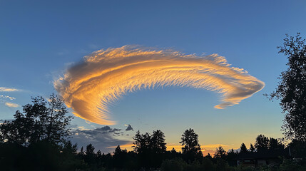 A dramatic sunset sky showcases clouds forming a giant bow over a tranquil landscape with silhouettes of trees
