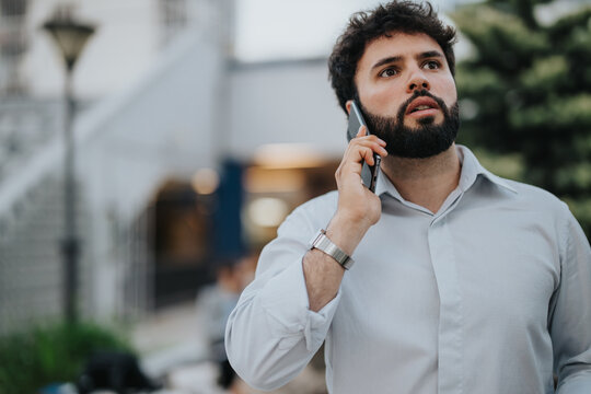 Concerned young man in a white shirt having a serious phone conversation while walking outdoors in an urban environment.