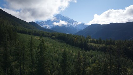 A breathtaking scenic view of Mount Rainier in the distance, surrounded by rolling forested hills and a lush green valley.