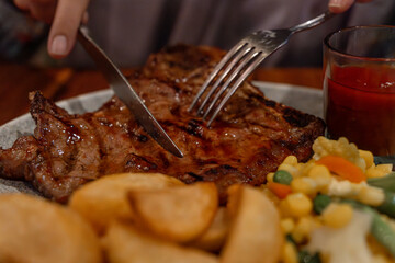 person eating T-bone steak with a BBQ sauce and potato wedges