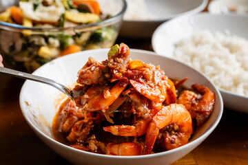 Spicy shrimp soup in a white bowl on a wooden table, udang balado,