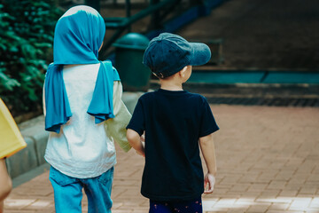 Brother and sister, with their backs to the camera, holding hands, muslim kids