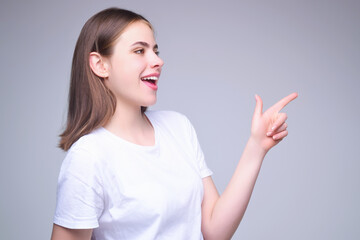 Young woman pointing copy space. The point. Studio portrait of Girl looking at camera and pointing away on gray isolated background. Finger point gestures.