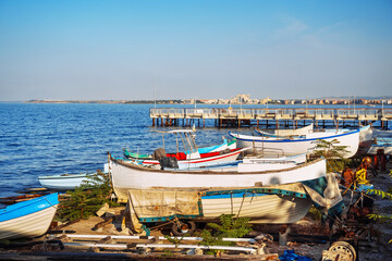 Obraz premium Brightly colored fishing boats are lined up along the shore, with a wooden pier extending into the serene sea.