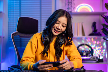 Asian young beautiful woman playing game on smartphone in neon room. 