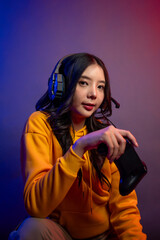 Asian young woman wearing headphones, playing games in neon background. 