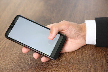 Man unlocking smartphone with fingerprint scanner at wooden table, closeup