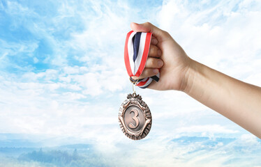 Woman holding bronze medal in hand against sky, closeup