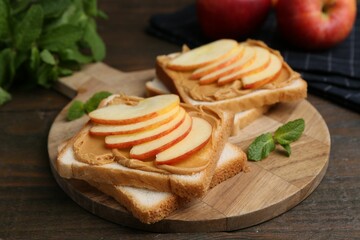 Tasty sandwiches with peanut butter, apples and mint on wooden table, closeup