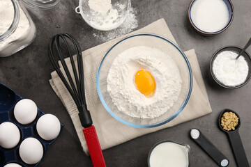 Baking powder with egg yolk in bowl surrounded by other products on grey textured table, flat lay