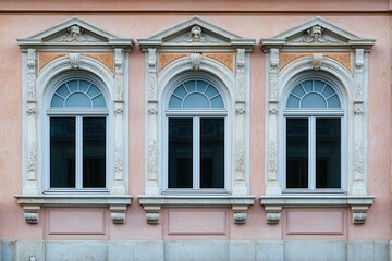 Three arched windows with ornate frames on a pink building facade.