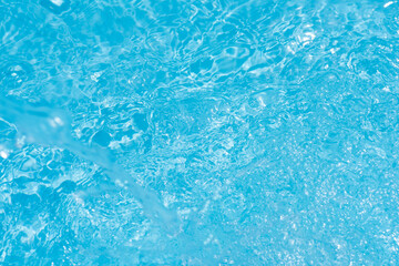 Blue water with ripples on the surface. Defocus blurred transparent blue colored clear calm water surface texture with splashes and bubbles. Water waves with shining pattern texture background.