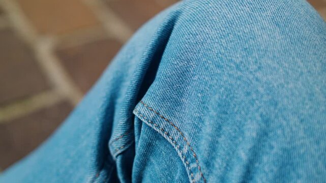 A ladybug rests on blue jeans, flying off, set against a blurred outdoor background