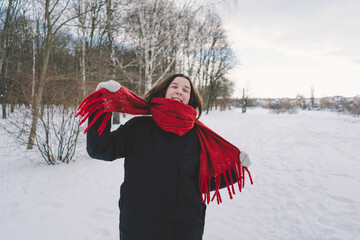 A smiling woman with a red scarf enjoys a snowy winter day in a serene forest setting beneath a...