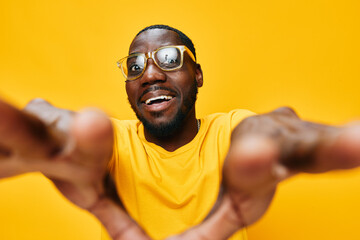 happy man in yellow t shirt with glasses expressing joy against a vibrant yellow background, smiling widely and reaching out with hands for an engaging and playful concept
