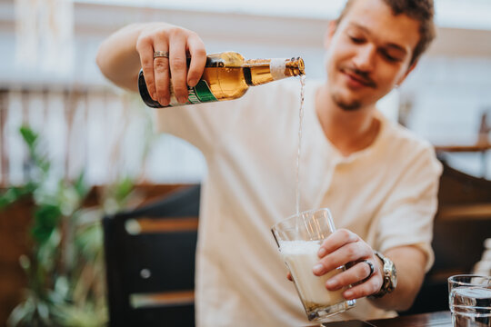 A relaxed young man is seen pouring a bottle of cold beer into a glass. The setting is casual, evoking a friendly and leisurely atmosphere perfect for social gatherings.