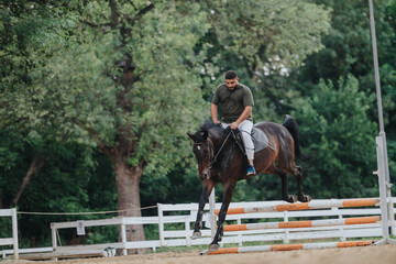 Man showcasing equestrian skills as he rides a horse jumping over a barrier in a park setting.