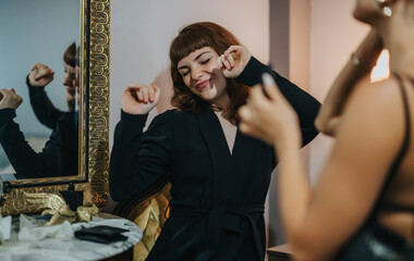 A woman in a black outfit joyfully dances in front of a decorative mirror, expressing happiness and relaxation at home.