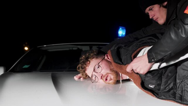 Slow motion shot of a man being arrested by police on the hood of the car
