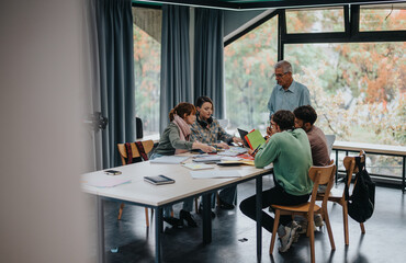 A group of university students working together on a project in a spacious classroom, guided by...
