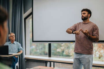 A young man presenting to a small audience in a modern office environment. A seated listener pays...