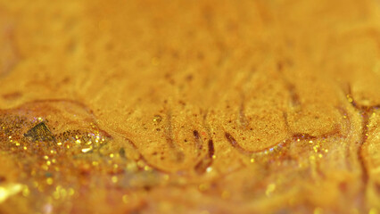 Shiny paint spill. Liquid glitter flow. Defocused golden color metallic sequin particles wet gloss acrylic fluid wave abstract art background with bokeh lights.