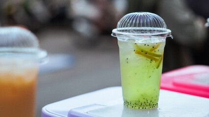 Close up A glass of fresh green drink with pieces of fruit, served with ice cubes in a plastic cup.