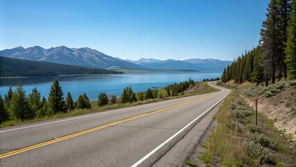 Obraz premium A peaceful scene of an empty asphalt road running alongside a lake or ocean with mountains visible in the distance under a clear blue sky, serenity, ocean, calmness