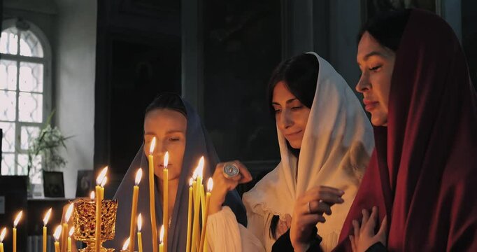 Christian Women engage in peaceful prayer with candles, creating atmospheres for deeper inner peace, stronger spiritual connections. Beautiful Christian women cross themselves in prayer before altar