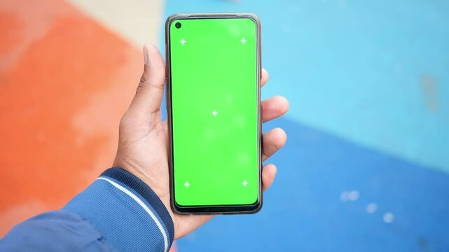 A hand holds a smartphone with a green screen outdoors, highlighting current tech trends