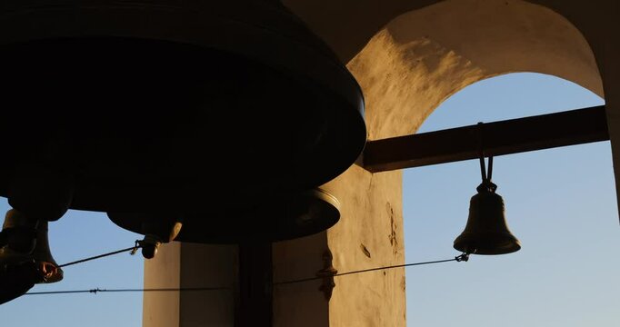 In grand church tower, bell ringer begins sacred ritual. Silhouetted bells at sunset symbolize connection across generations, preserving religious heritage alive to this day. Church, Faith, Spiritual