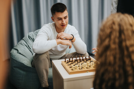 A group of teenagers engage in a friendly chess game indoors, focusing on strategy and concentration in a casual environment. Perfect for themes of leisure, youth, and strategic thinking.