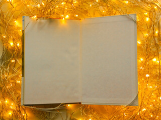 An open notebook with white pages on a background of bright yellow garland lights. Background, place for text. Drawing up new goals is a concept.