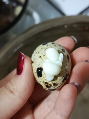 The egg white leaked out during cooking. A woman's hand holds a quail egg. Boiling soft-boiled eggs for breakfast is a concept.