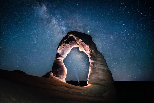 Man flashing light underneath Delicate Arch in Arches National park under the Milky Way night sky