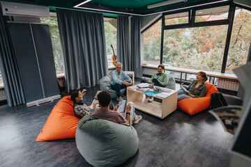 A professor and students share ideas in a stylish study lounge with large windows and comfortable...