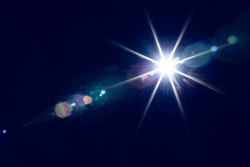 Bright shining light illuminating dark space with lens flare effects creating vivid star-like patterns in darkness.