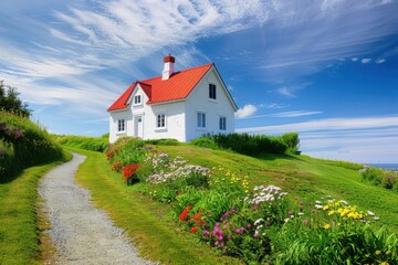 Fototapeta premium A charming white house with a red roof surrounded by colorful flowers and a scenic pathway.