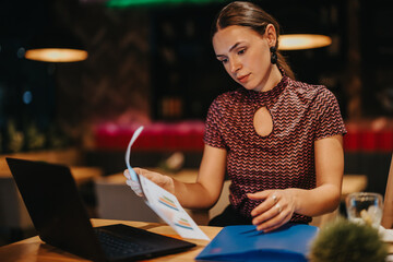 A dedicated businesswoman reviews documents while working late at night in a modern office setting....