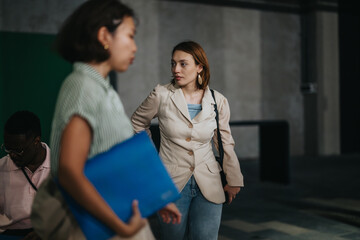 Professional woman in a beige blazer walks with confidence in a modern office. Background colleagues highlight teamwork and collaboration. The image captures focus and business environment.