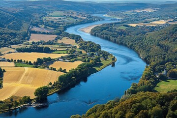 A scenic river winding through lush green fields and hills under a clear blue sky.