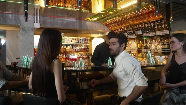 VIP group guest siting fronted bar discussing lifestyle travel with friend or couple with mixed punch cocktail on bartender preparing drink backside decorated Christmas tree on counter bar. Vinosity.