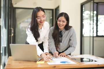 Happy Asian business people working together using laptop and tablet in office.