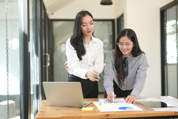 Happy Asian business people working together using laptop and tablet in office.