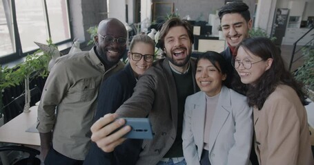 Multiethnic group of businesspeople having fun in office taking selfie with smartphone camera laughing grimacing. Business and photo concept.