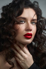 woman with beautiful curly hair poses elegantly, accentuating her striking features with bold red lips in a soft-lit environment, creating an enchanting atmosphere