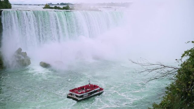 tour boat filled with passengers in red ponchos nears the base of Niagara Falls, surrounded by mist and cascading water, capturing thrill of exploration and natural grandeur. tour boat with passengers
