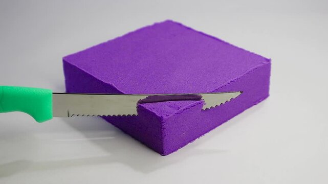 Video of purple kinetic sand in the shape of a square that is cut using a super sharp knife 