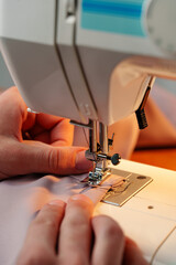 Hands sewing fabric using a sewing machine on a wooden table in a well-lit workspace